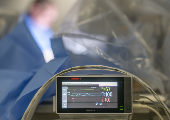 HF-Messungsgerät zeigt verschiedene Werte während einer OP die verschwommen im Hintergrund zu sehen ist