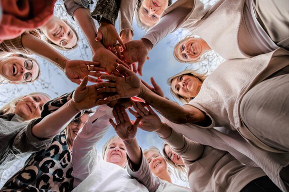 Team der Hebammen strecken Ihre Hände in die Mitte. Das Bild wurde von unten geschossen und man sieht das gesamte Team. 