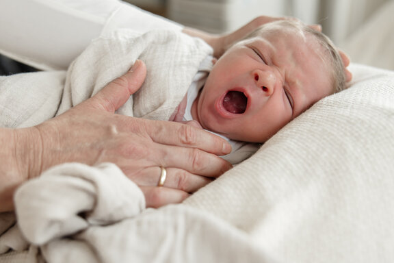 Neugeborenes Kind liegt auf einer Decke und wird von zwei Händen stützt 