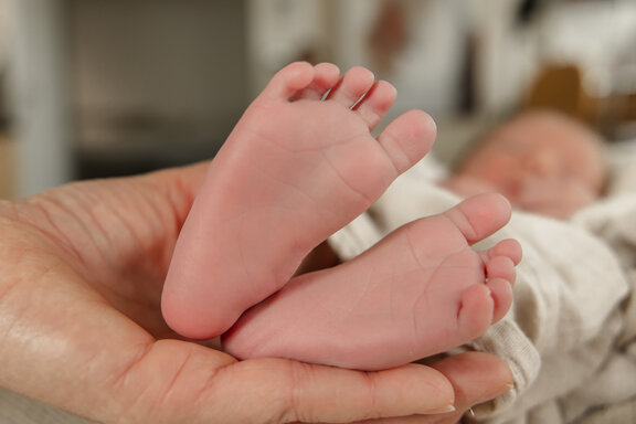 Eine Hand hält die Füße eines Neugeborenen fest.