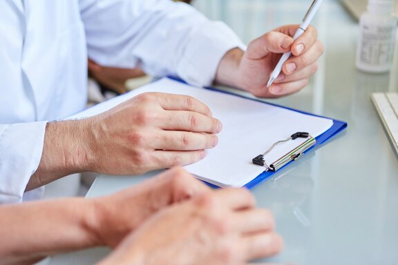 ein Patient sitzt mit dem Arzt am Tisch während eines Anamnesegesprächs und füllen ein Dokument aus