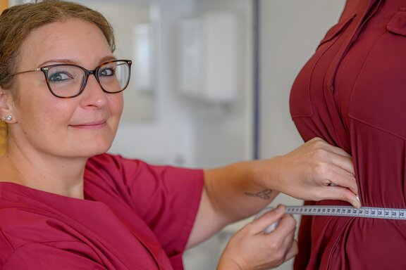 Mitarbeiterin im Lipödem Department misst den Bauchumfang einer Patientin mit einem Maßband. Dabei schaut sie in die Kamera.