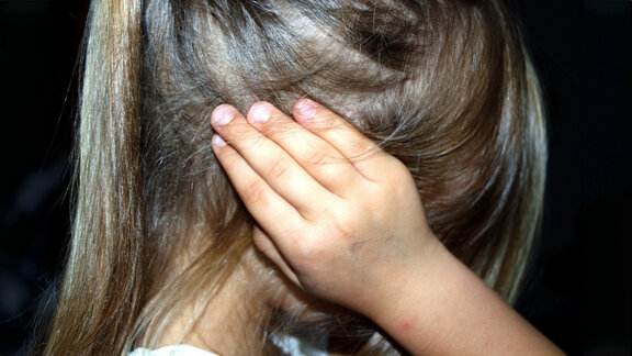 Junges Mädchen hält sich die Ohren zu. Man sieht das Kind von der Seite als Beispiel für die Kinderschutzambulanz.
