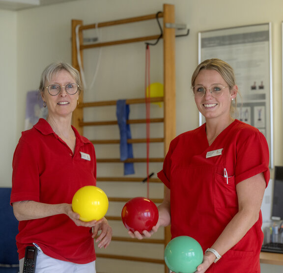 Zwei Ergotherapeutinnen stehen in einem Geräteraum und halten Bälle in der Hand.