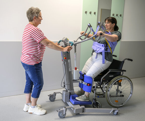 Pflegeüberleitung steht mit Patientin, die gerade eine Übung macht, an einem Geriatrischem Gerät.