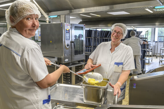 Küchenmitarbeiter bereiten das Mittagessen vor und schauen dabei in die Kamera.