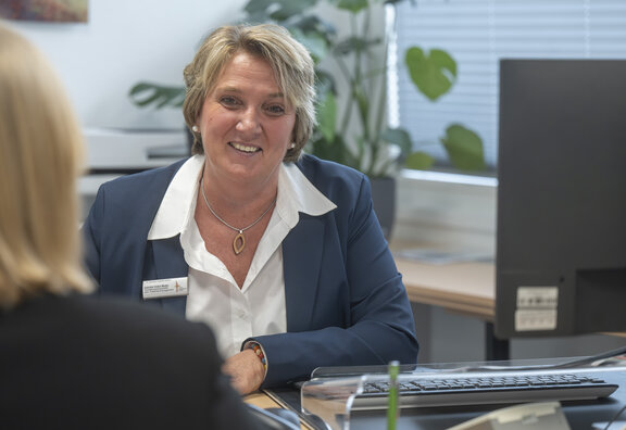 Mitarbeiterin nimmt eine Patientin im Büro auf und lächelt dabei in die Kamera