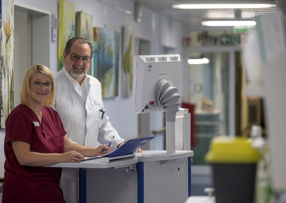 In der Klinik für Altersmedizin steht Chefarzt Dr. med. Frank Kuczera am Visitenwagen mit einer Pflegekraft auf dem Flur der Station.